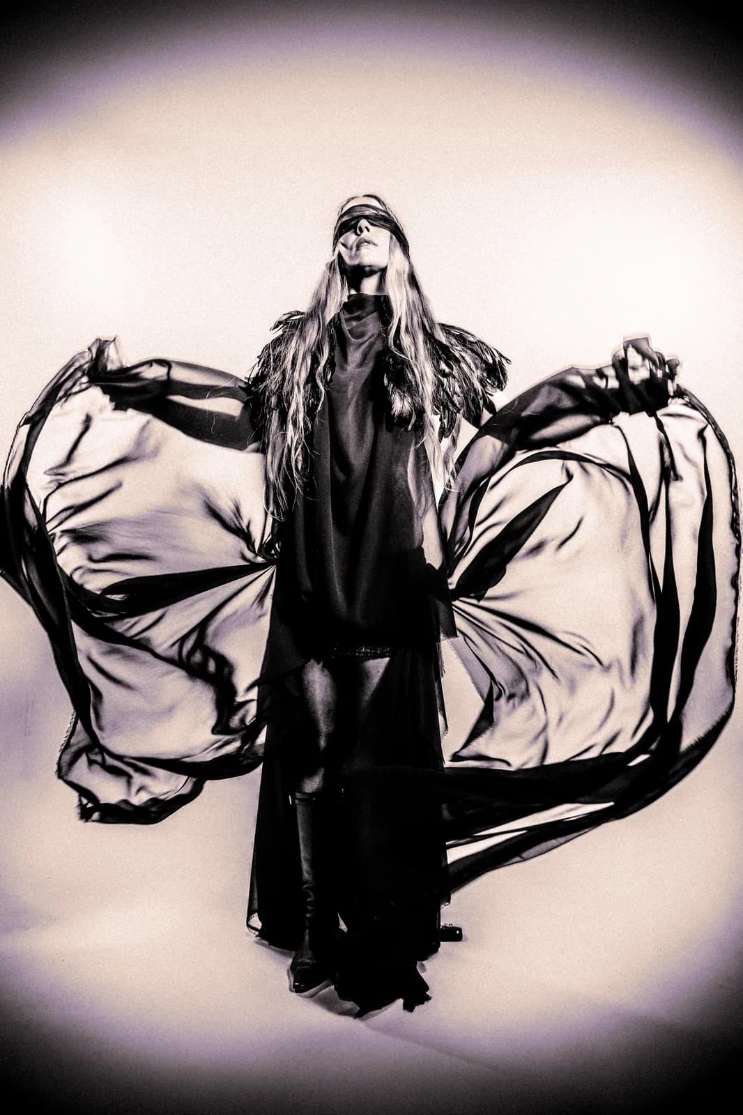 PYTKO, blindfolded, holding out a sheer black cape